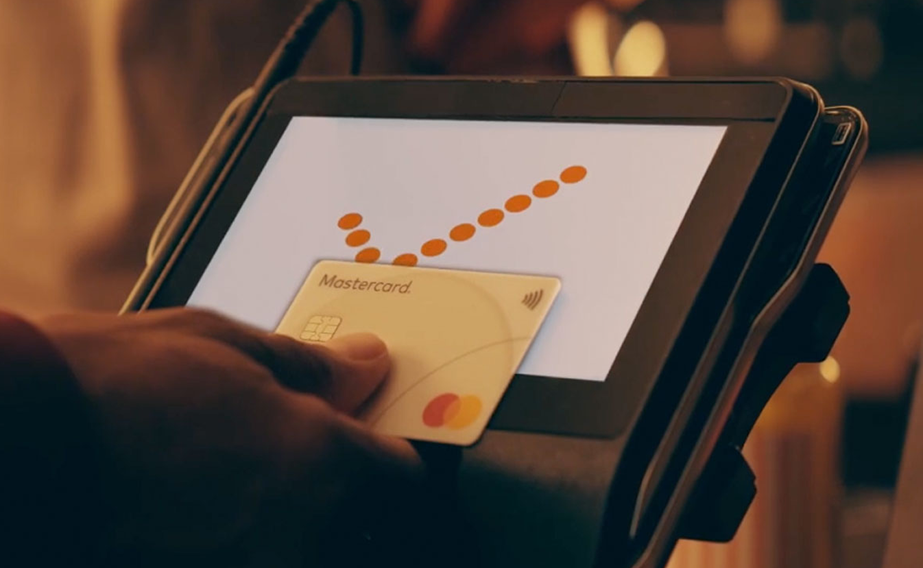 A close-up of a hand completing a contactless transaction with a Mastercard, showing how easy it is to tap to give for a cause. 