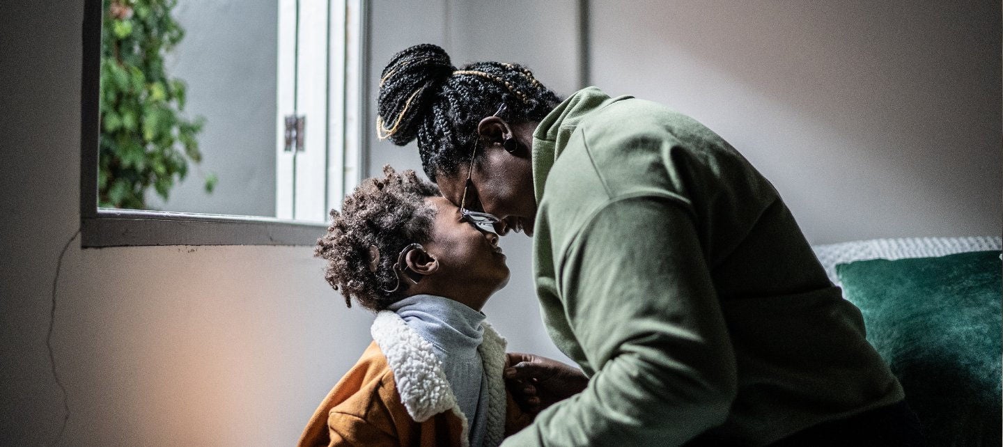A mother and her young son touch foreheads in a living room. 
