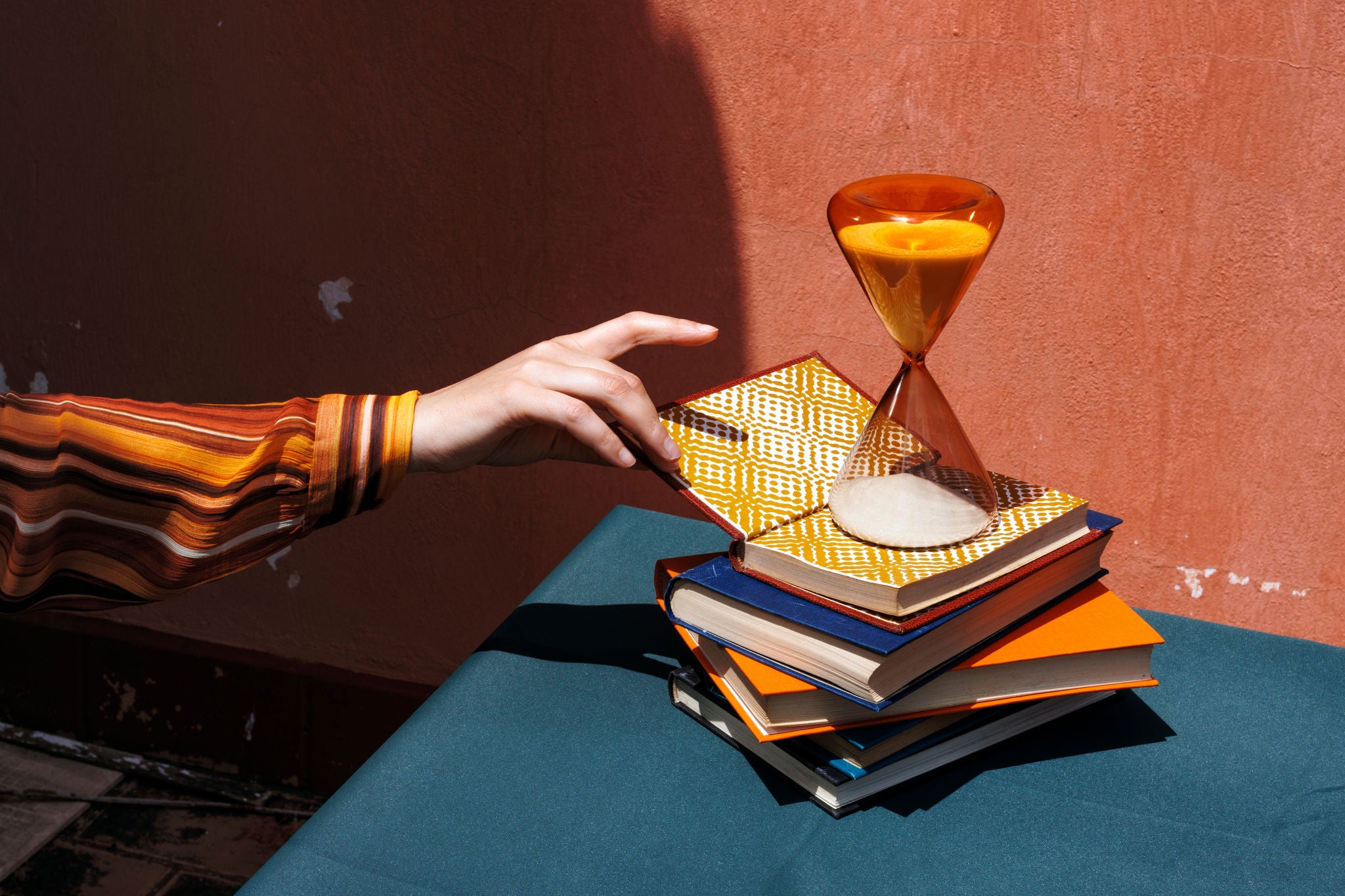 Hand reaching for a book on a stack with an hourglass on a table