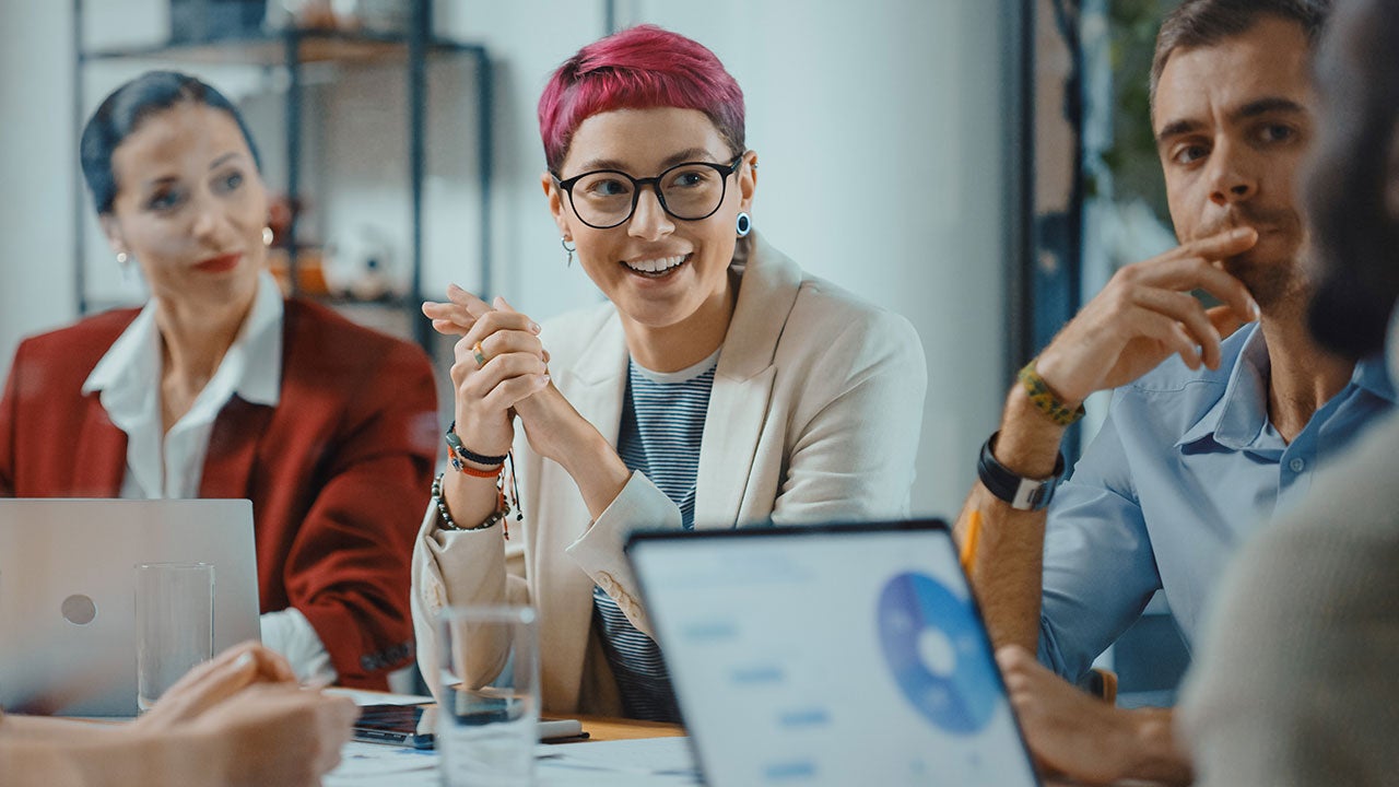 Specialist with short pink hair talks about firm strategy with diverse team.