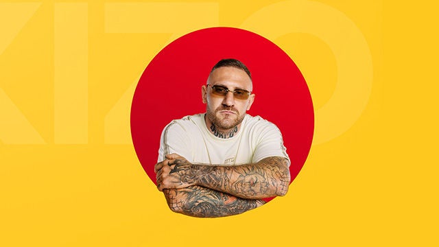 Mężczyzna z tatuażami i okularami przeciwsłonecznymi na tle czerwonego koła.