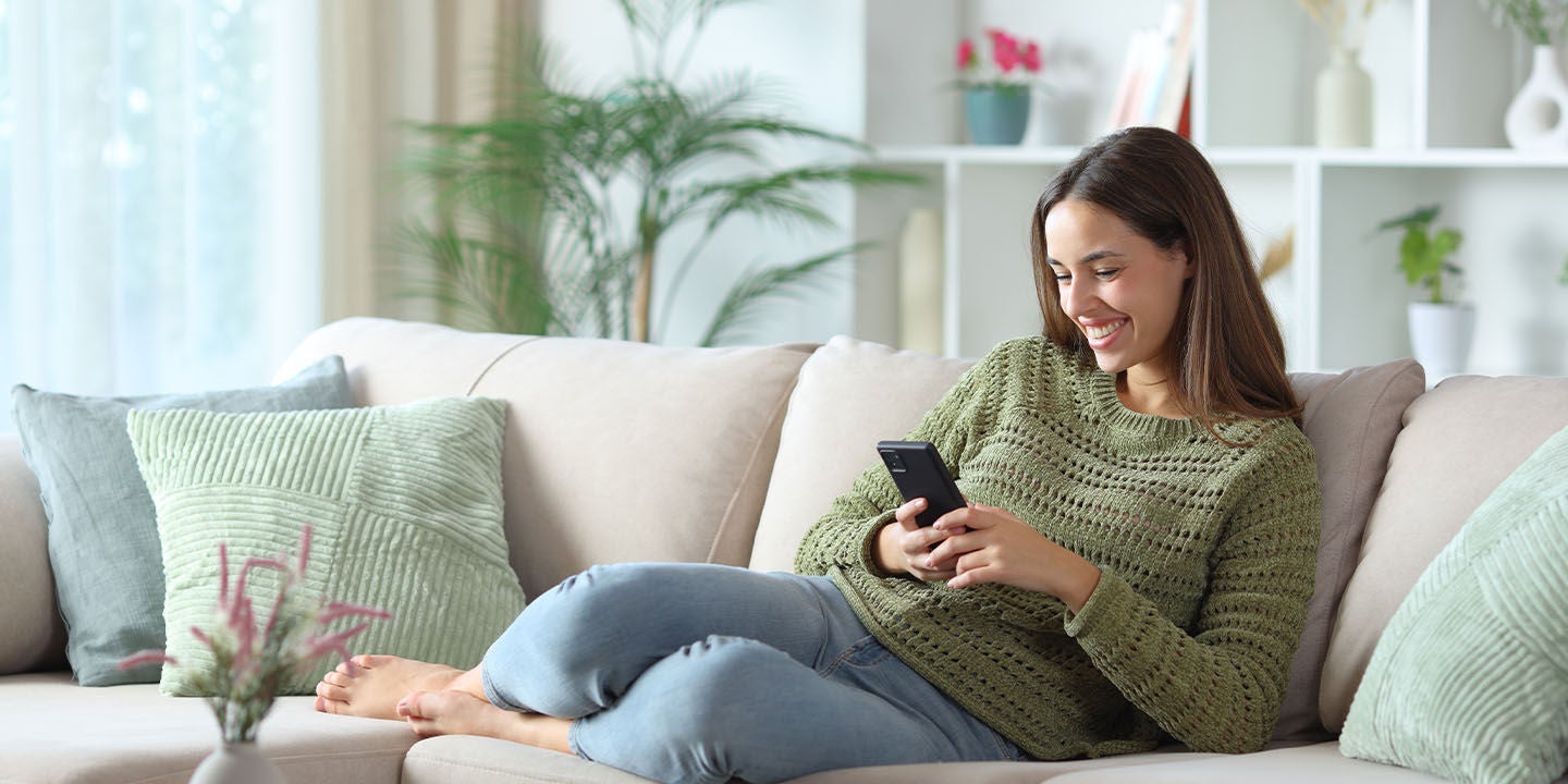 Woman using her smartphone while laying on the sofa