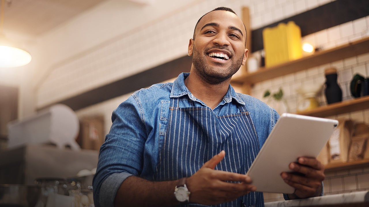 Smiling man in apron taking orders in cafe.