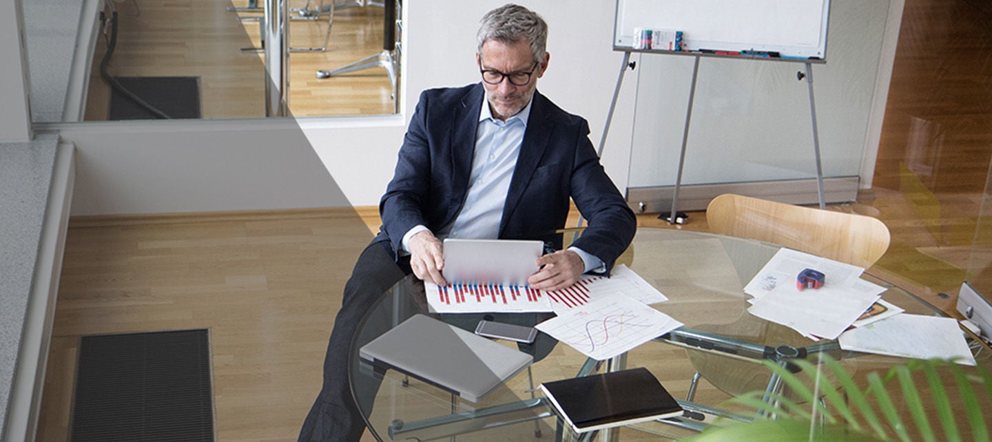 Eldre mann iført dress jakke sitter foran laptop analyserer grafer og dokumenter.