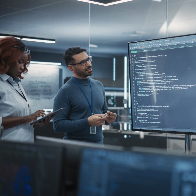 Colleagues look at a large screen with coding on it in an office. 
