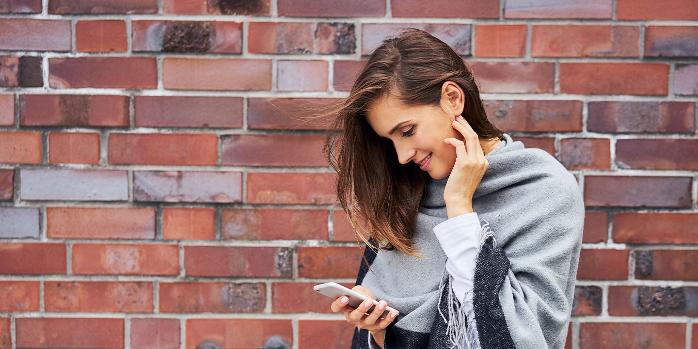 Woman using a phone next to a brick wall