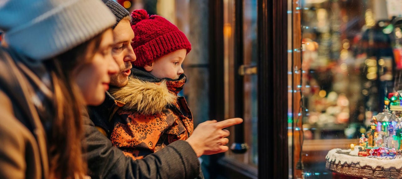 A family dressed in winter gear looks at a store window with Christmas decorative scenes. 