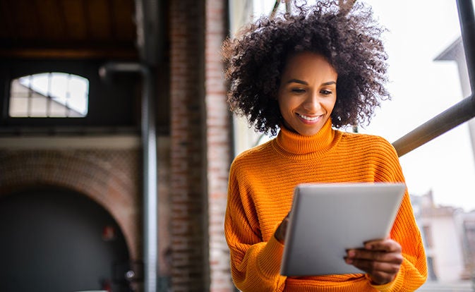 Woman in an orange sweater using a notebook computer indoors.