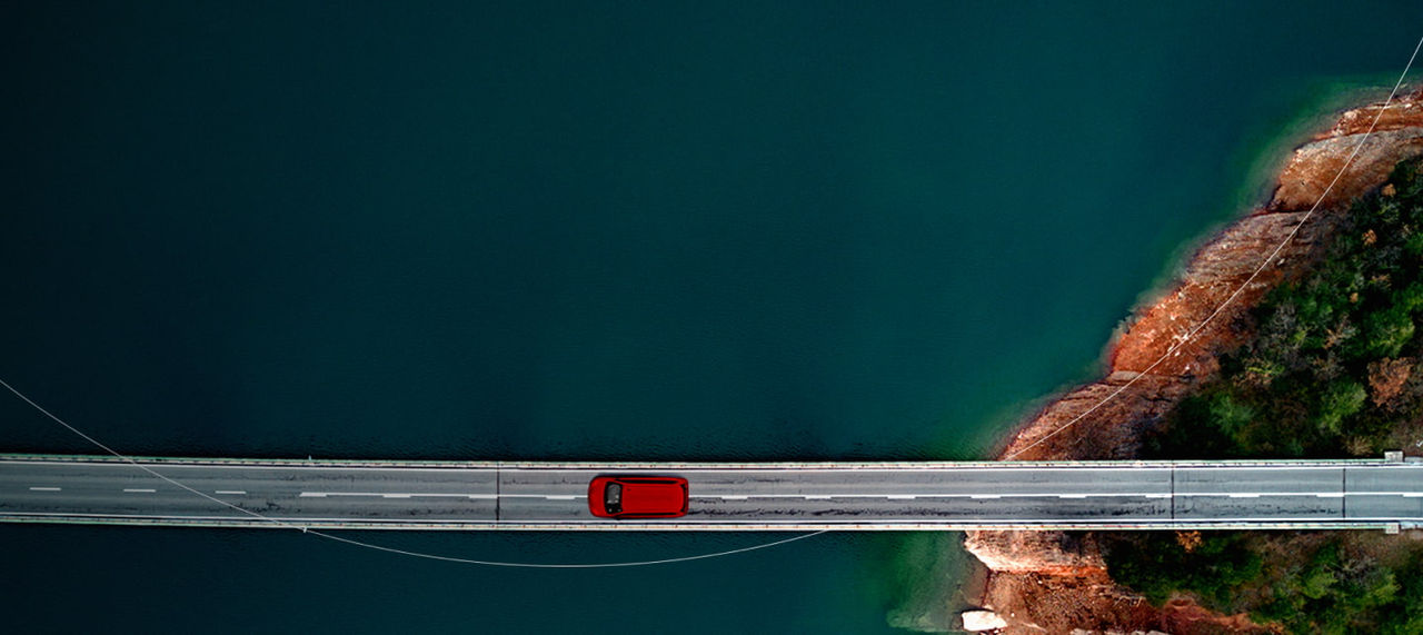 red car driving across a long narrow bridge