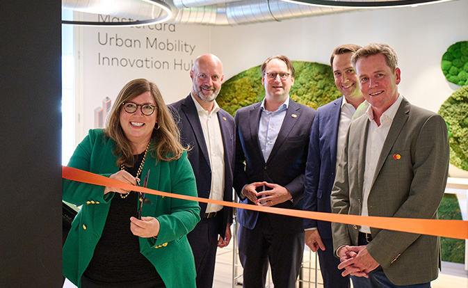 Cinco personas en la ceremonia inaugural del Centro de Innovación de Movilidad Urbana de Mastercard, mujer cortando una cinta naranja.