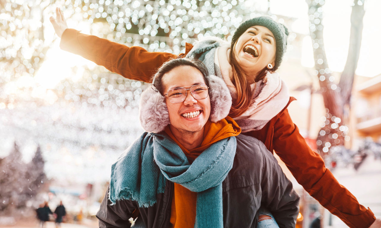 Multiracial couple in love wearing winter clothes celebrating Christmas holiday - Husband and wife having fun hanging out together walking on city street - Winter holidays and relationship concept