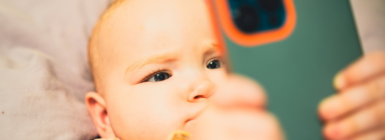 Ein Baby liegt auf dem Rücken und schaut auf ein Smartphone. 