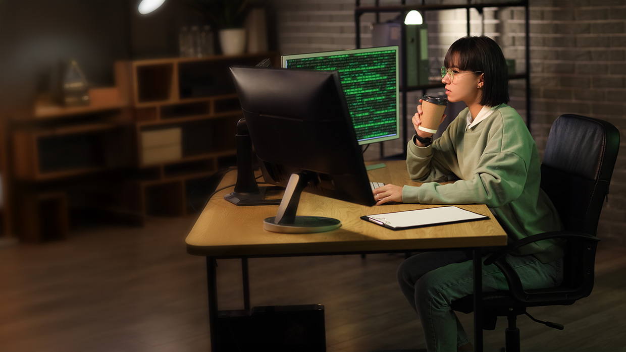 Woman programmer with coffee cup working in office at night.