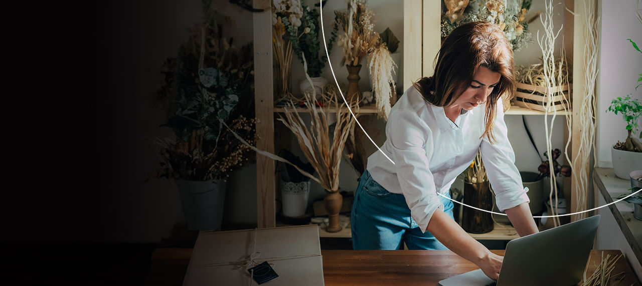 Žena je fokusirana na svoj laptop, okružena raznovrsnim biljkama u živopisnoj cvjećari.