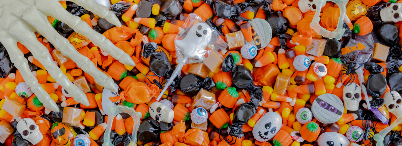 Brightly-colored Halloween candy spread out on a table with a plastic skeleton hand reaching over the candy.