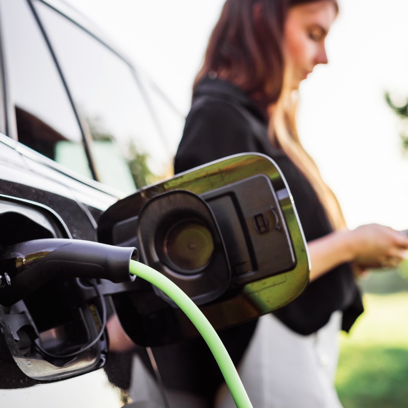 A woman looks at her smartphone while her car is EV charging. 