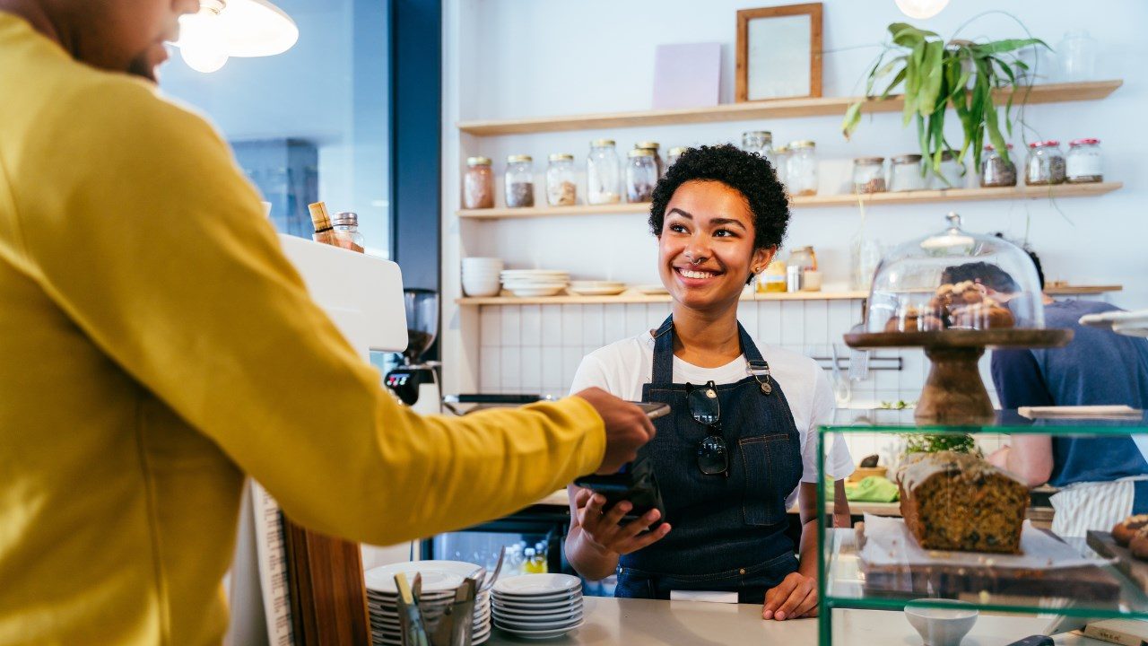 Un caissier en tablier prend un paiement numérique d’un client. 