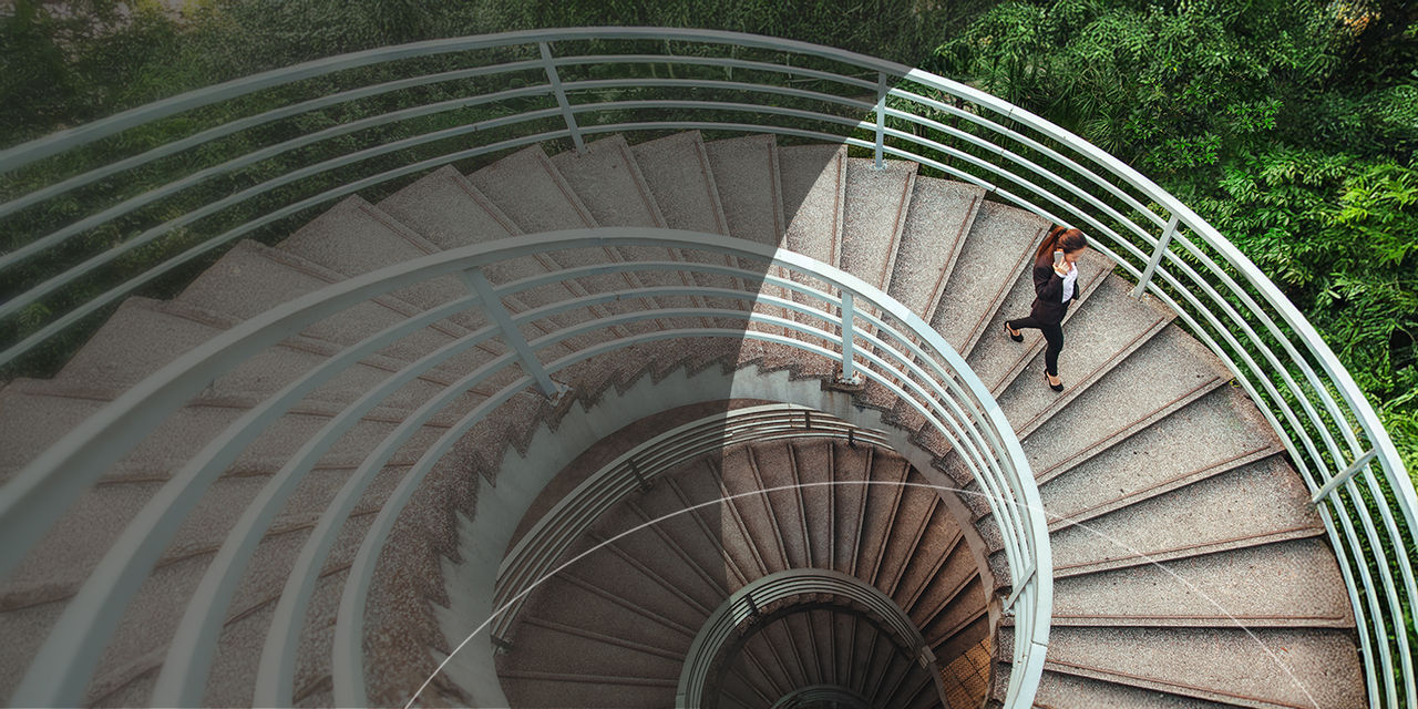 Une personne descend un escalier en colimaçon, les courbes élégantes de l'escalier et l'architecture environnante étant mises en valeur.