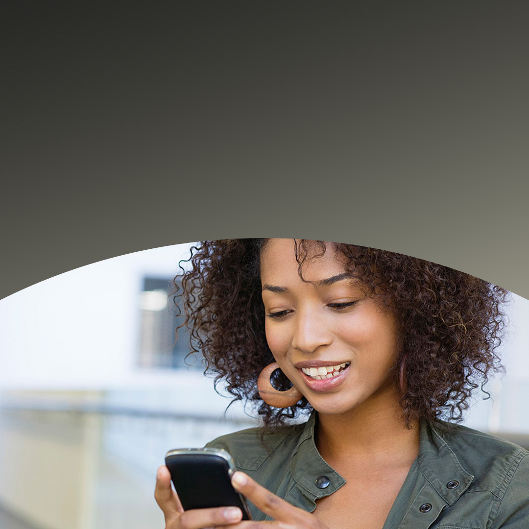 Une femme souriant en regardant son smartphone.