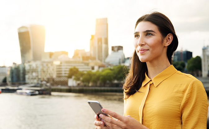 Jonge vrouw die een telefoon vasthoudt met stadslandschap op de achtergrond.
