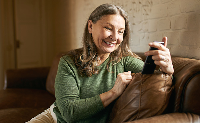 Mulher sorrindo enquanto olha para o smartphone em casa.