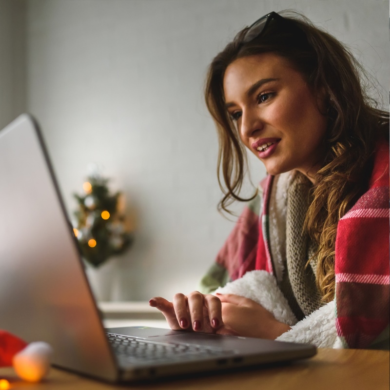A woman looks at her laptop in a room decorated for the holidays. 