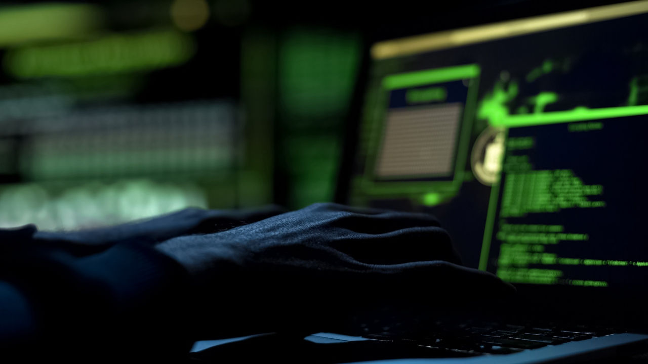 A computer screen in a darkened room with a person' shand on the keyboard. 
