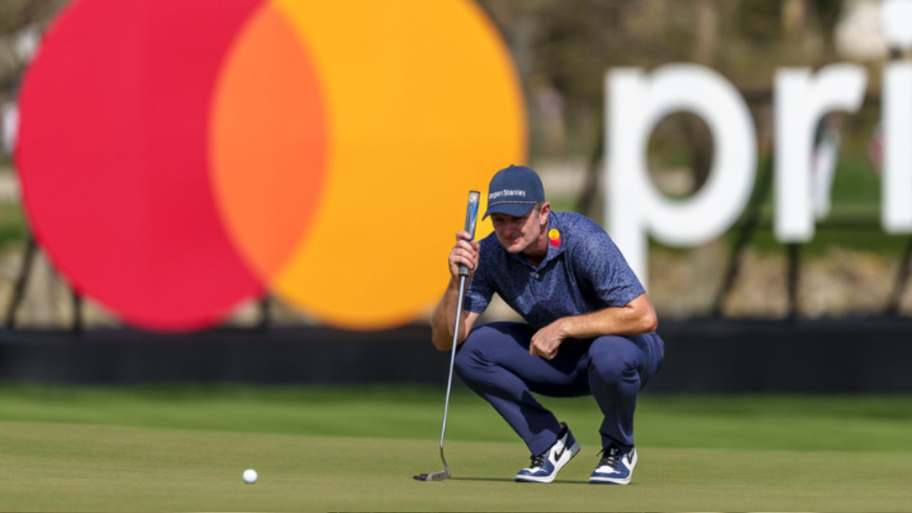 Justine Rose crouches on a green and eyes a golf ball in front of Mastercard's logo. 
