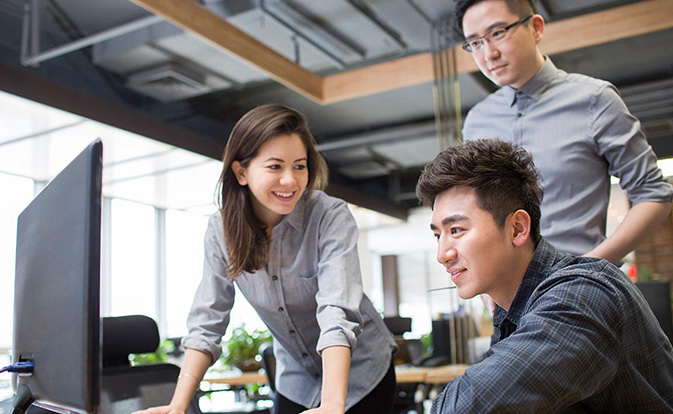Three employees collaborating in an office, focused on a computer screen.