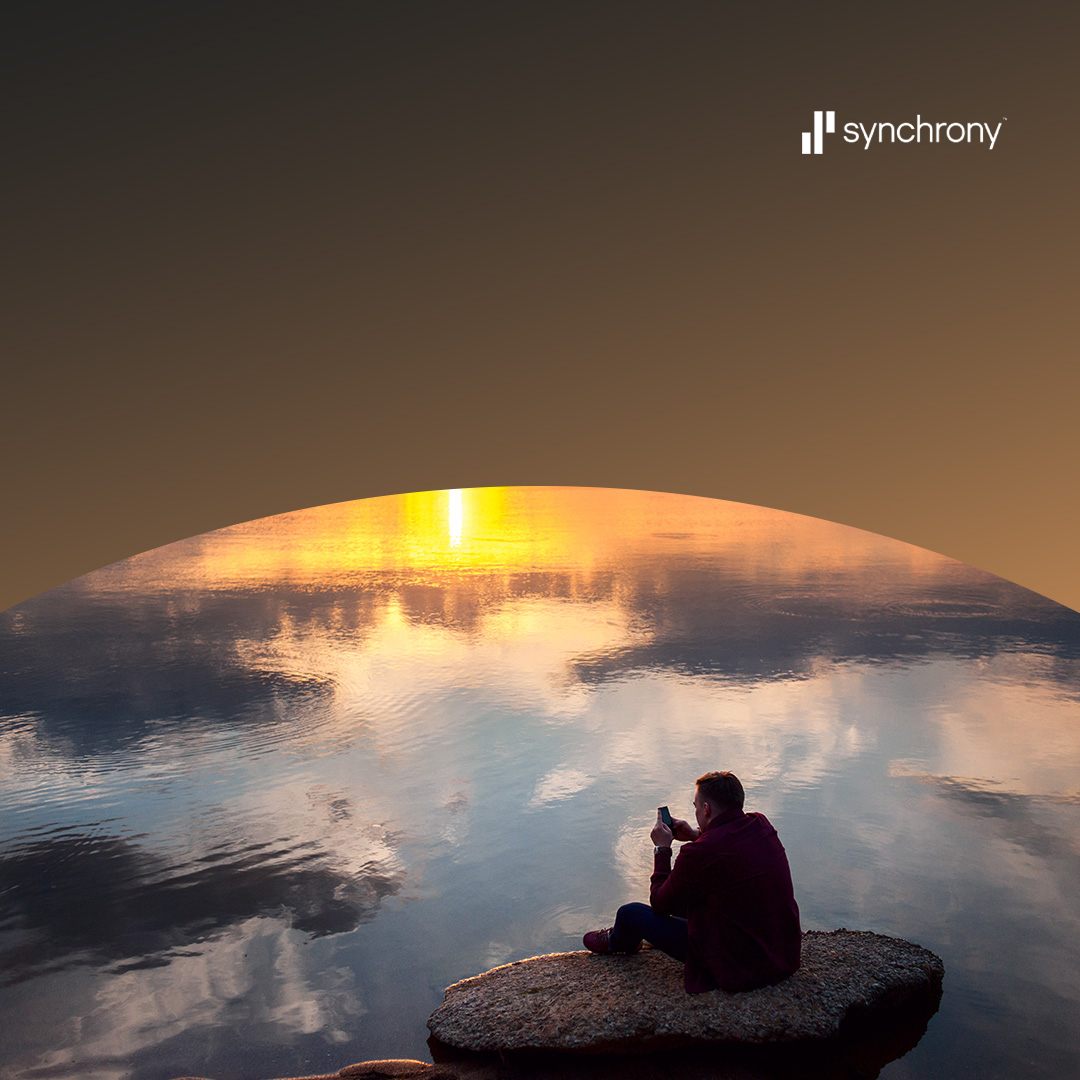 Un homme assis sur un rocher au bord du lac au coucher du soleil.