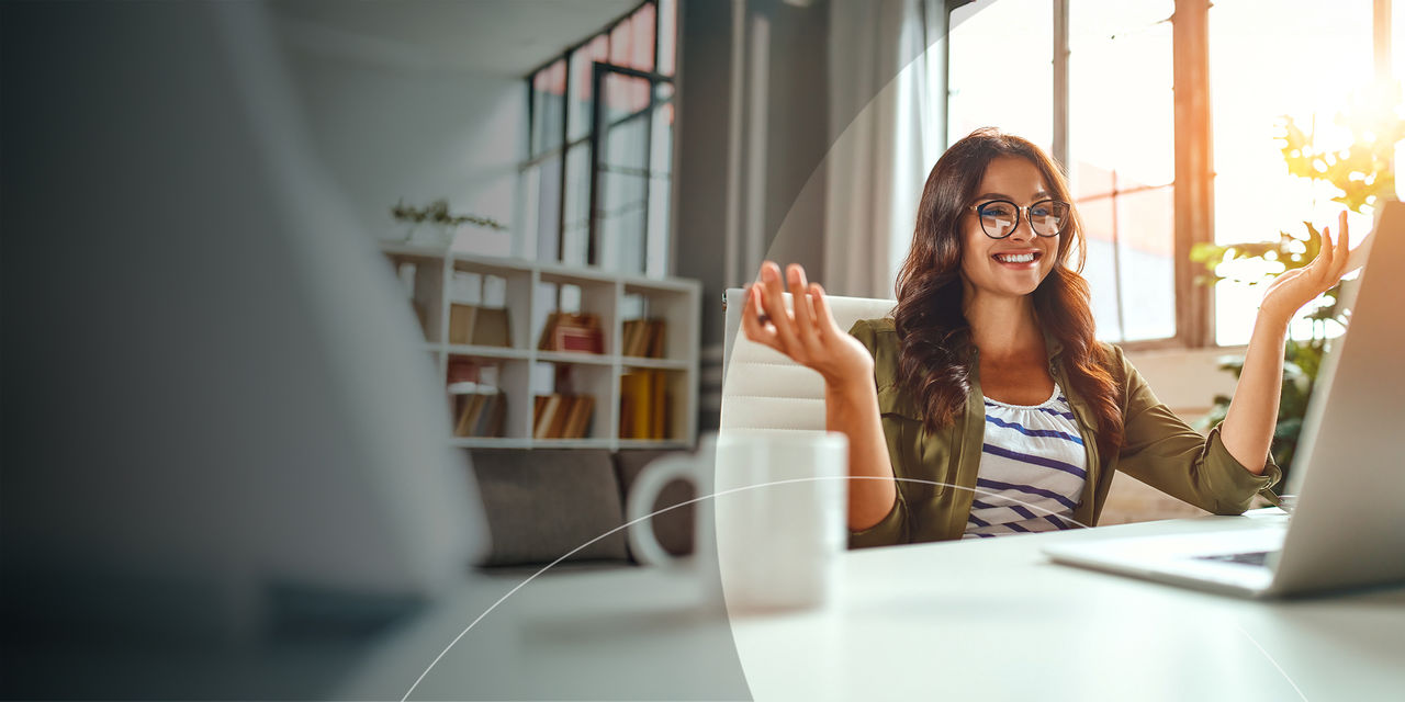 Une femme assise à un bureau, les mains levées, regardant son ordinateur portable, exprimant de l’excitation ou de la surprise.