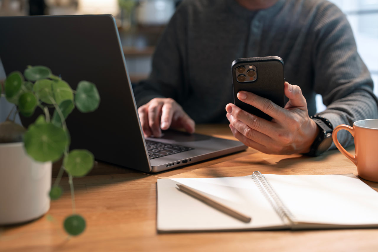 Man holding phone device and using laptop.