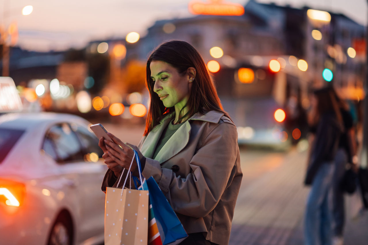 Woman standing on sidewalk at twighlight looking at phone.