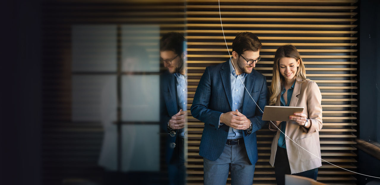 Two people engaged in discussion while looking at a tablet in an office space.