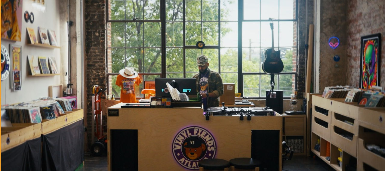 DJ Silver Knights looks at his computer among his record collection in front of a large window. 