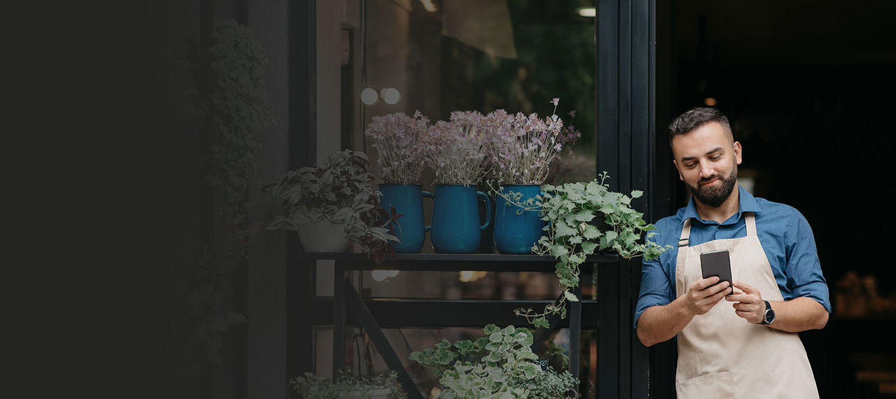 Dueño de una floristería de pie fuera de la tienda con un teléfono.