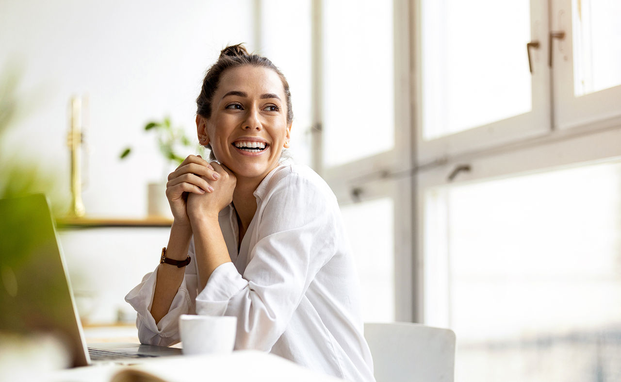 A woman seated at a desk, focused on her laptop while working in a well-lit office environment.