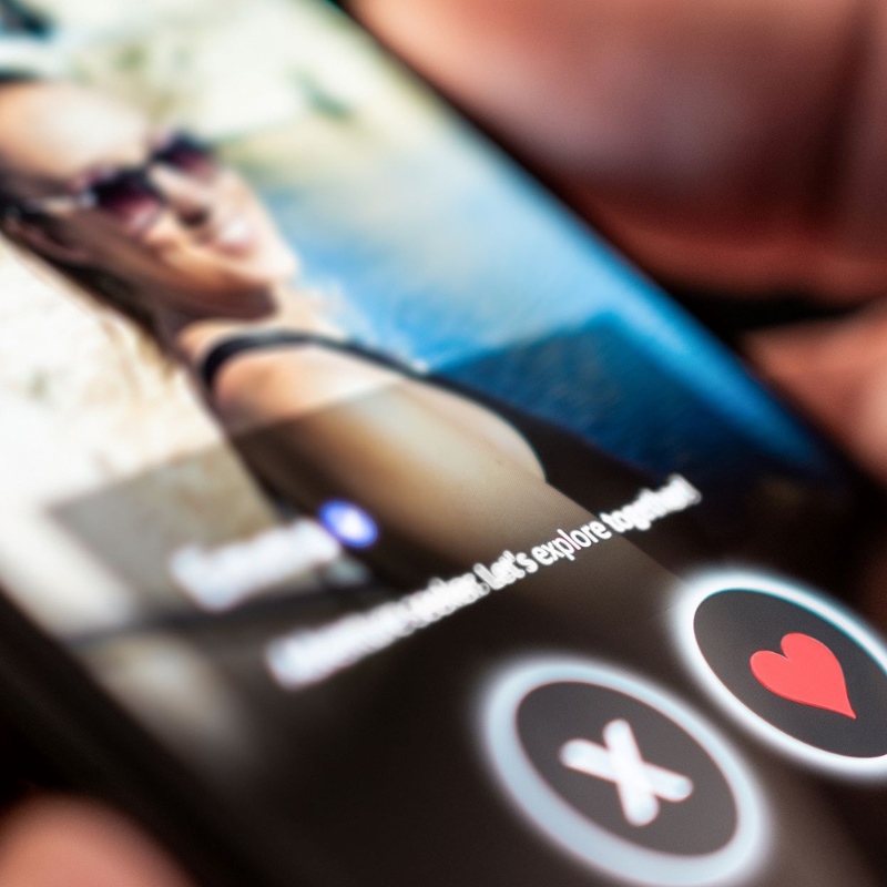 A person holds a smartphone with a dating app open on it. 