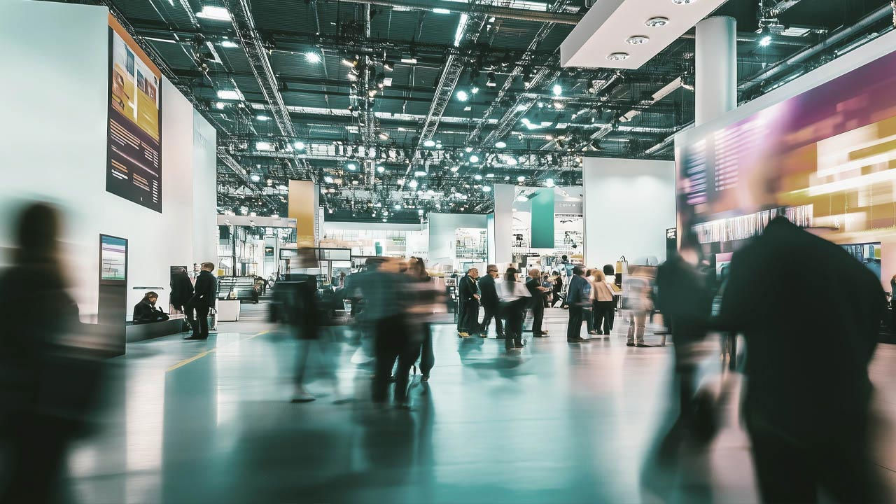 Ein verschwommener Blick auf Personen, die durch eine volle Ausstellungshalle gehen.