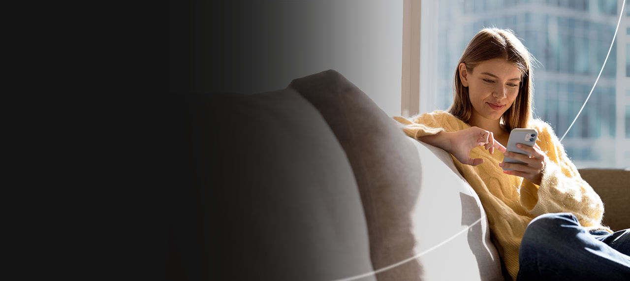 Frau sitzt auf dem Sofa und schaut auf ihr Handy.