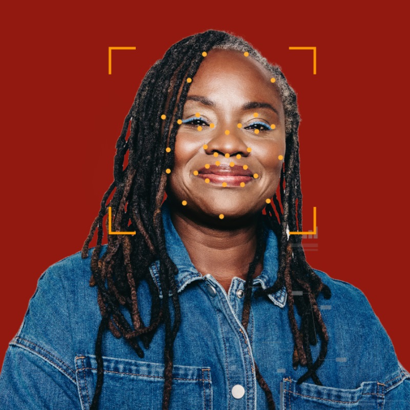 A woman with braids wearing a denim shirt smiles with an overlay showing biometric points on her face. 