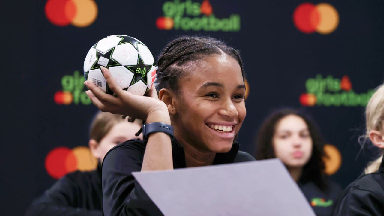 Jeune fille souriante tenant un ballon de football dans une classe.