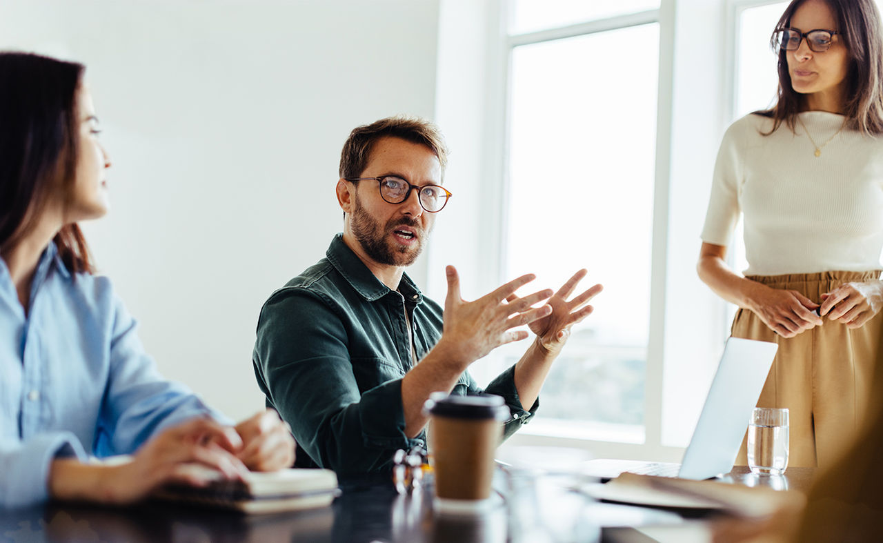 Un grupo de personas sentadas a la mesa, con un hombre que habla impetuosamente a los demás.