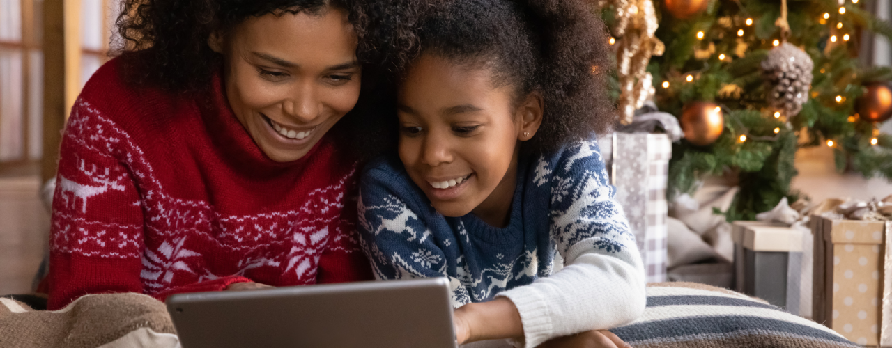 Una madre y una hija miran una tableta con un árbol de Navidad en el fondo