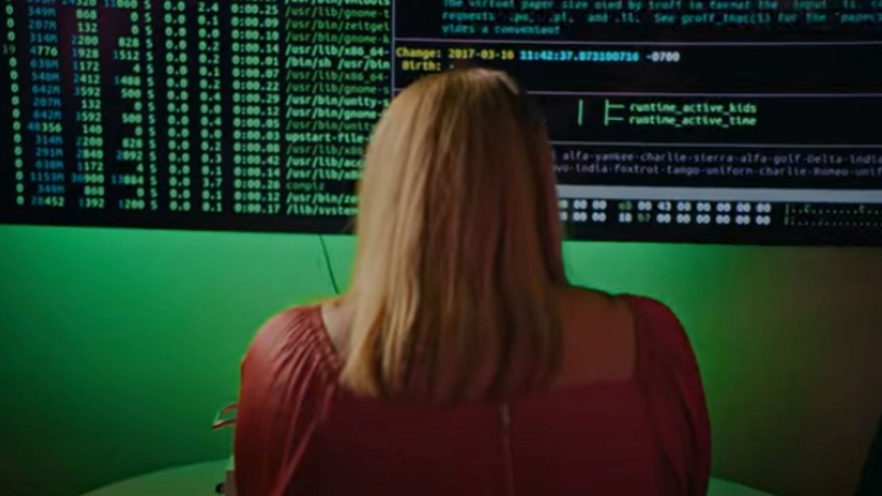 The back of a woman's head looking at a large computer screen with coding on it. 