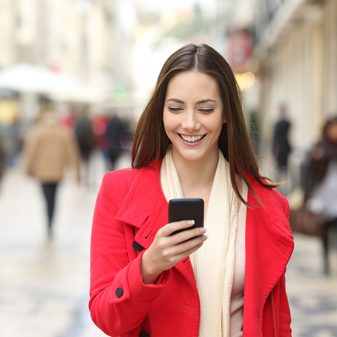 Girl in red over coat looking into mobile on street.