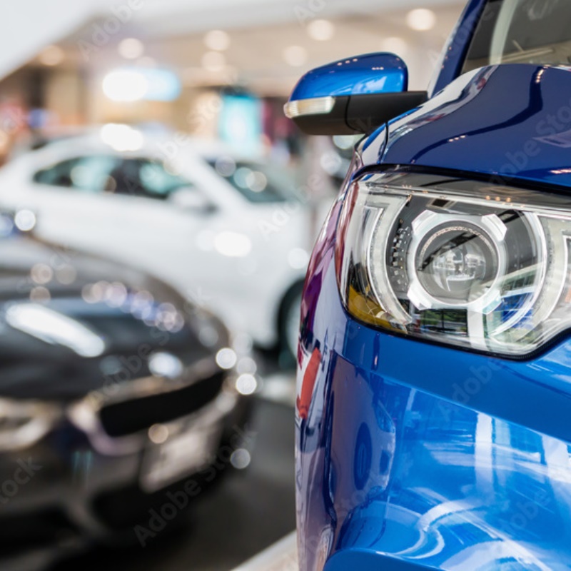 The front left of a car in front of other new cars in a dealership. 