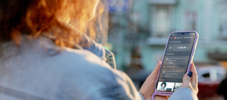 Lille virksomhedsejer omgivet af transportkasser, der betaler med telefon. 