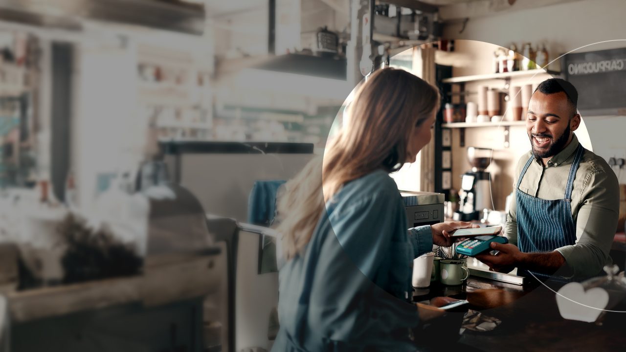 En kvinde, som betaler til en barista i en café ved hjælp af sin telefon.
