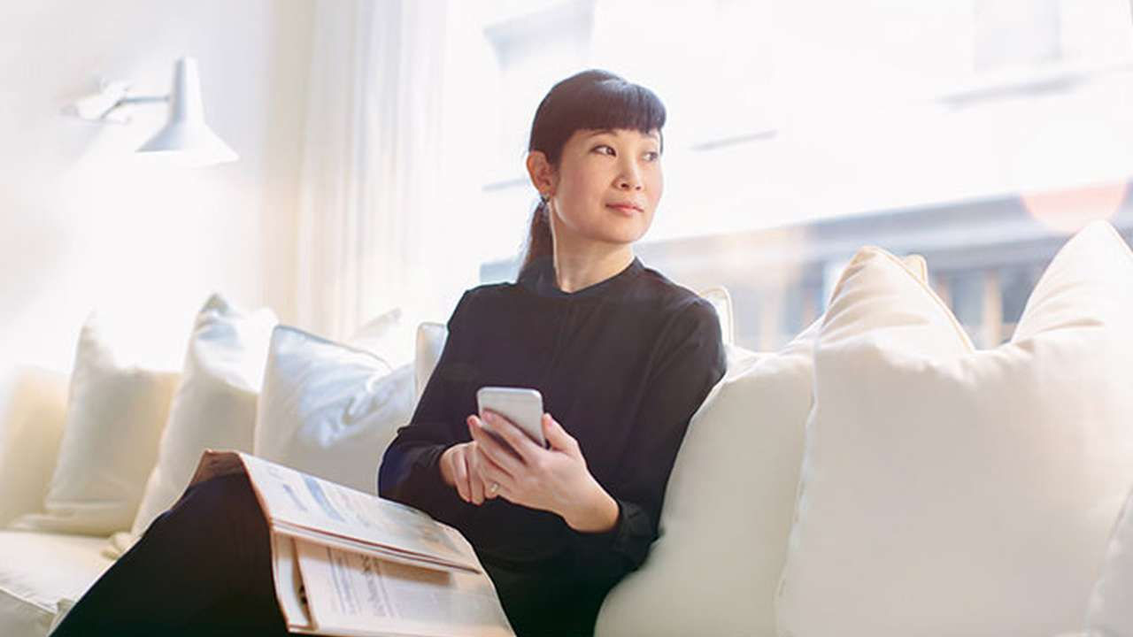 En kvinde sidder i en sofa med en mobiltelefon og et magasin.